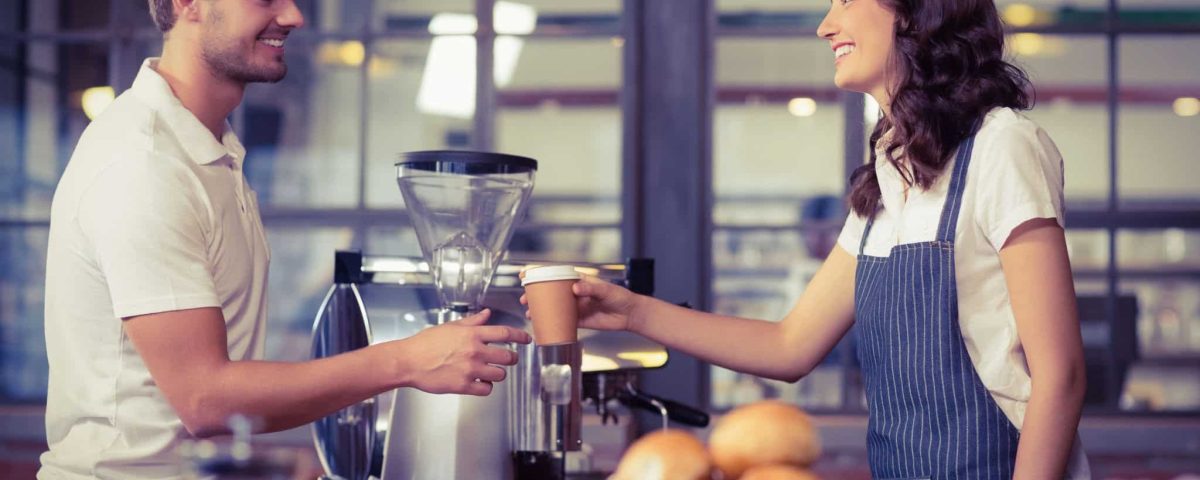 coffee shop worker handing a cup to a customer
