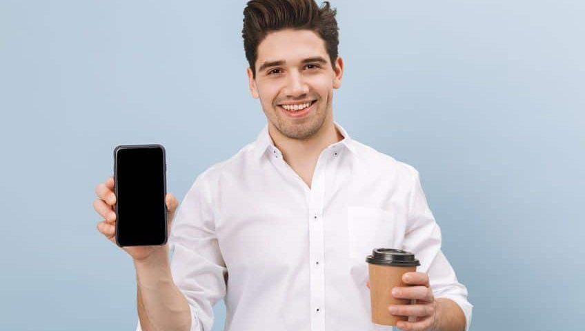 smiling man holding coffee and a phone
