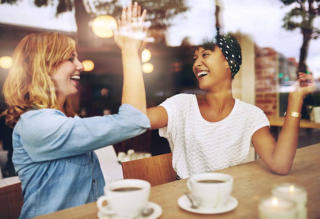 happy female friends high-fiving at a coffee shop
