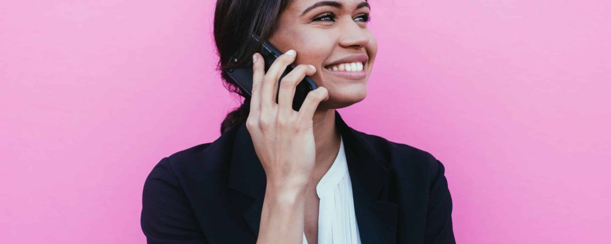 businesswoman smiling while on the phone, standing in front of a pink background