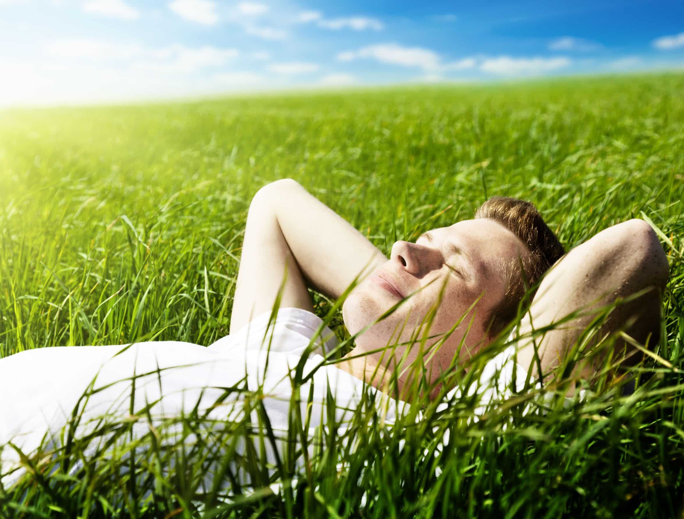young man closing his eyes and lying in a field of green grass