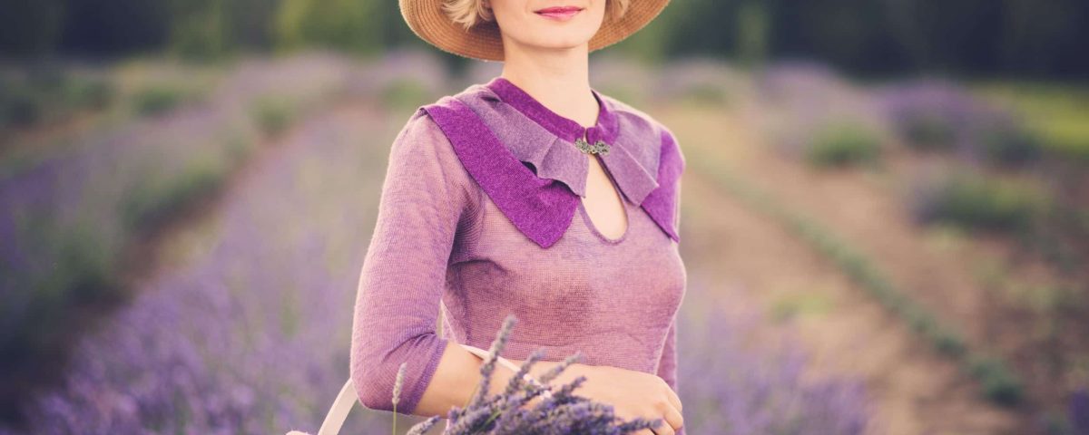 classy woman in a purple dress, standing in a field of lavender, with a basket of flowers