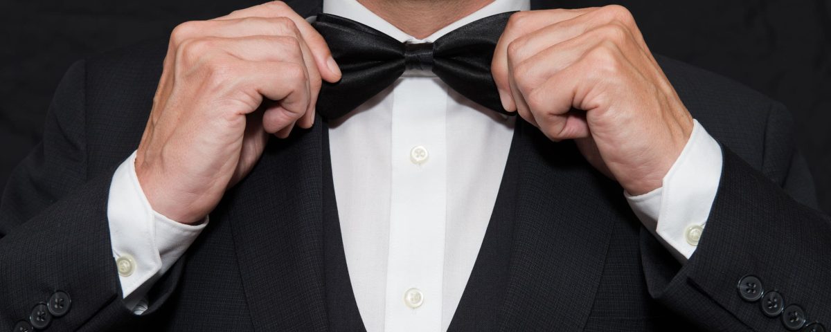a man in a black tuxedo straightening his black bowtie