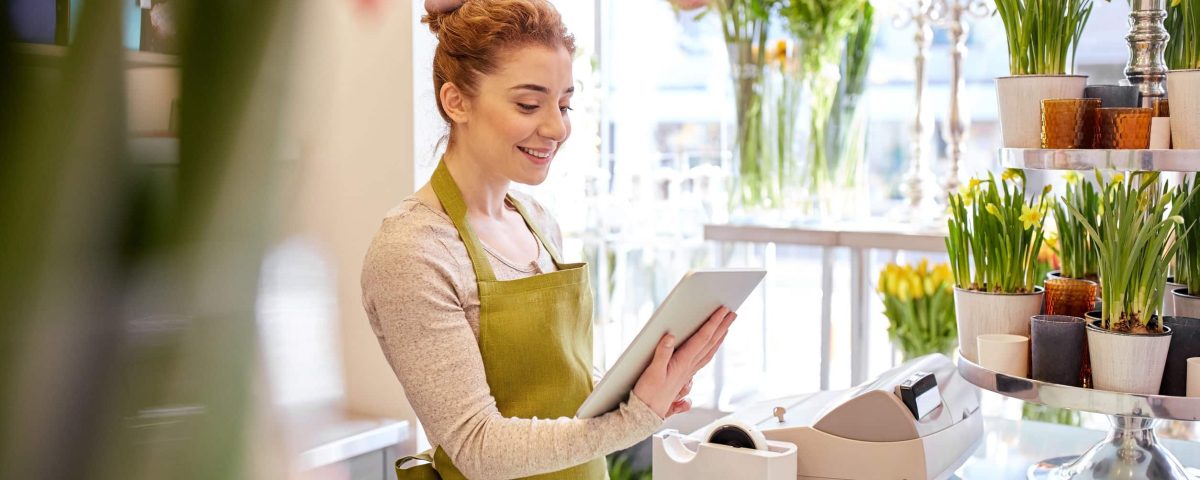 Small business owner checking her tablet, surrounded by flowers in a bright shop