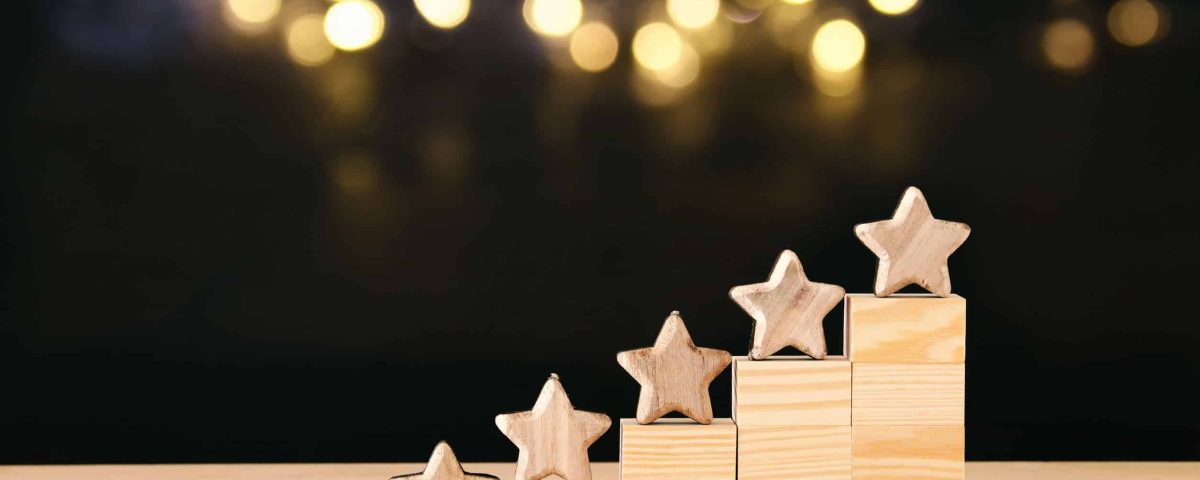 five stars on a mini wooden staircase with blurred lights on a dark background