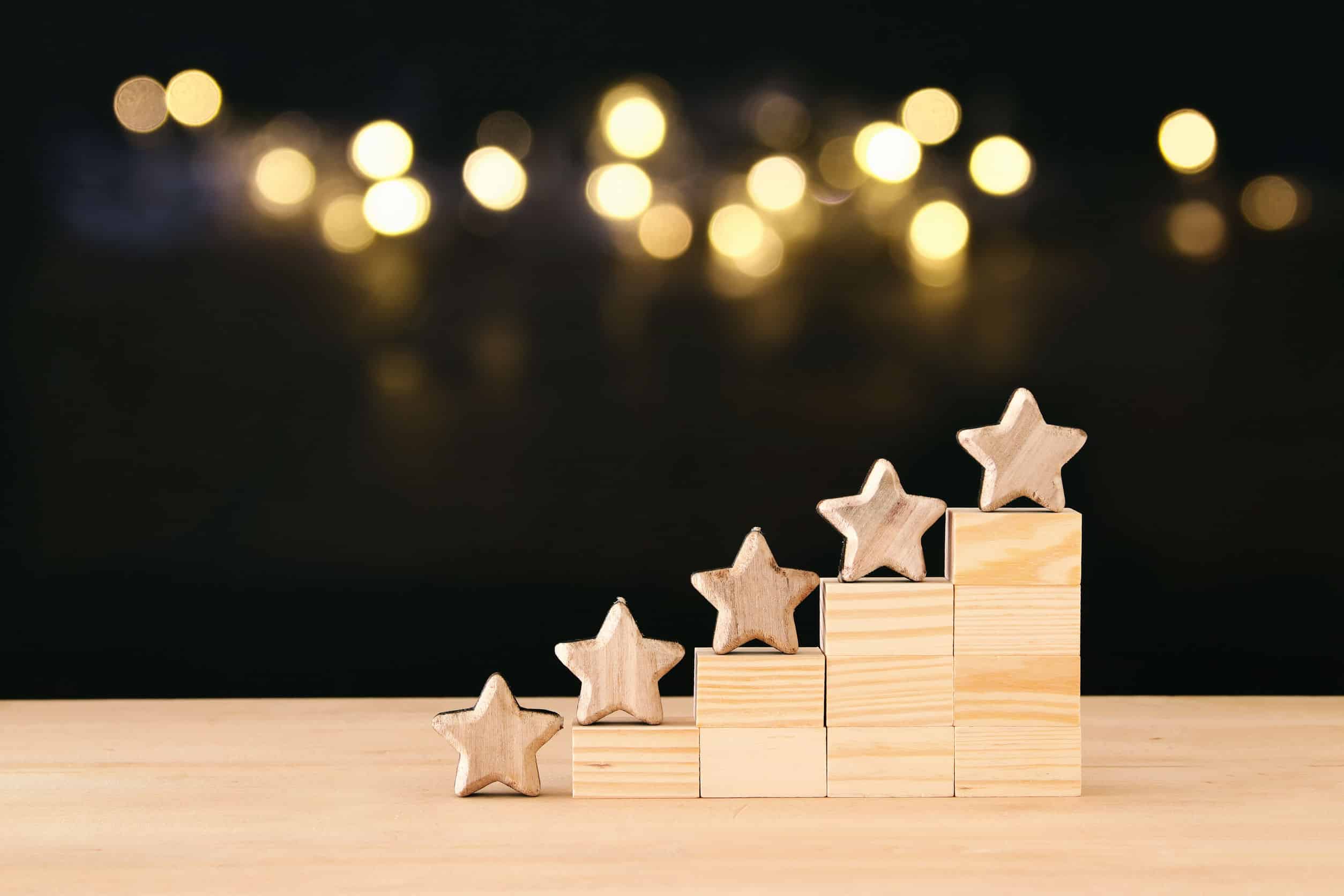 five stars on a mini wooden staircase with blurred lights on a dark background